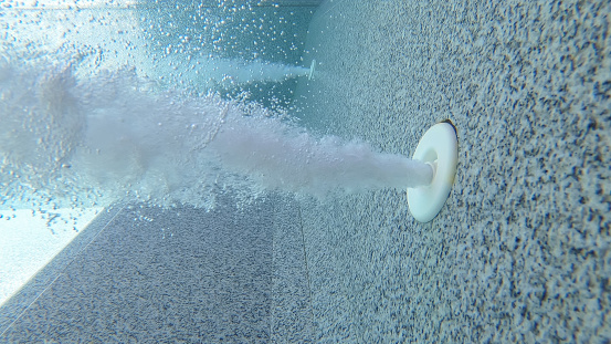 A nozzle blows jet air horizontally under water in swimming pool full with water.