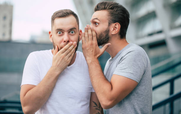 Two funny excited best friends in casual clothes are gossiping and chatting together outdoors. Two funny excited best friends in casual clothes are gossiping and chatting together outdoors. whisper men stock pictures, royalty-free photos & images