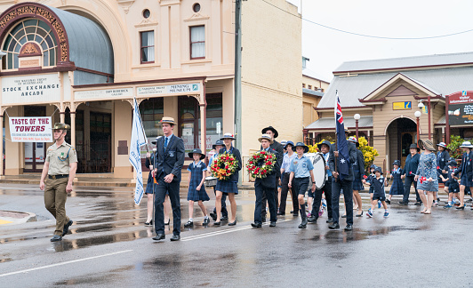 Charters Towers, Australia - April 25, 2019: School children marching in the rain on Anzac Day carrying wreaths and poppies