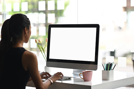 Una mujer está usando un ordenador de maqueta con pantalla vacía en el espacio de trabajo moderno. photo
