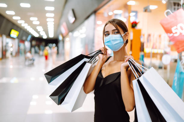 jeune femme dans le masque stérile protecteur de médicale sur son visage avec des sacs à provisions dans le centre commercial. - shopping mall shopping sale retail photos et images de collection