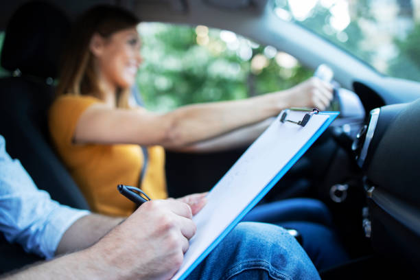 istock Close up view of driving instructor holding checklist while in background female student steering and driving car. Acquiring driver's license. 1270059193