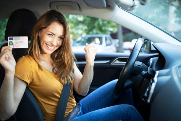 Car interior view of woman with driving license. Driving school. Young beautiful woman successfully passed driving school test. Female smiling and holding driver's license. stock photo