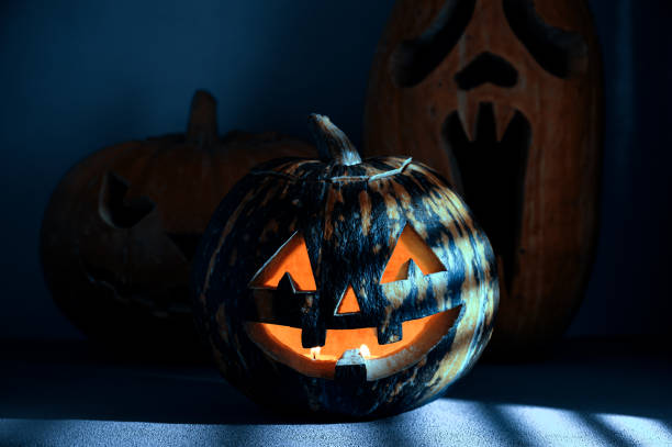 istock Halloween holiday background. Three Spooky Halloween pumpkins on the table, illuminated by moonlight through the jalousie. 1270060686