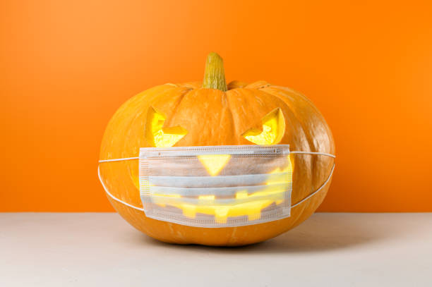 New normal concept. Glowing Halloween pumpkin in a protective medical mask on a orange background. stock photo