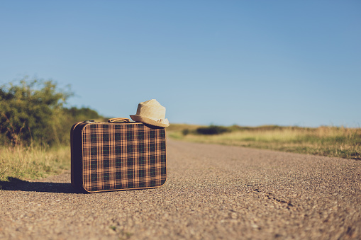 Image of old suitcase and hat on the country road.