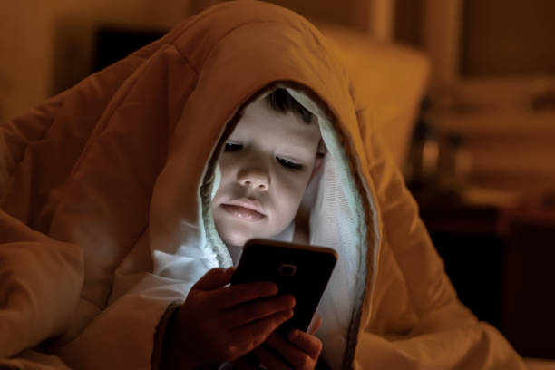 istock Boy laying in the bad while watching cartoons on mobile. 1270061159