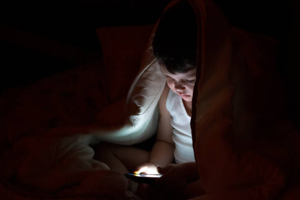 istock Curious boy sits in bed under white blanket and play games on smartphone. 1270061359