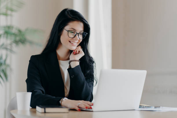 istock Cheerful female employee types on laptop computer, works remotely, concentrated with smile at device screen, writes email letter, works in office drinks coffee uses new application. Technology concept 1270062293
