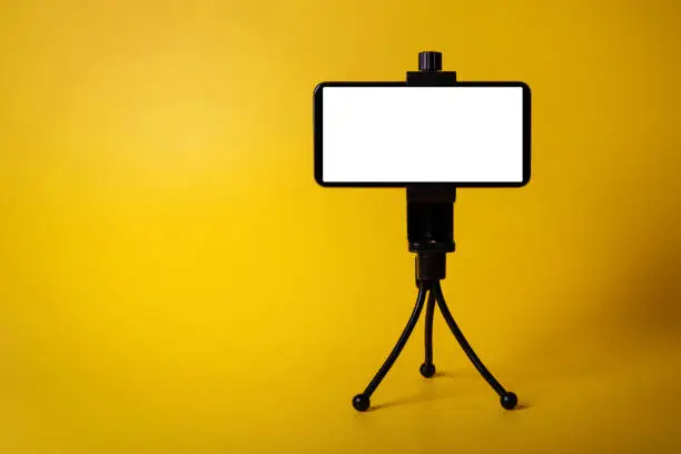mobile phone mounted on mini tripod with blank screen isolated on yellow background. copy space