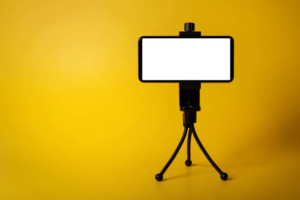 mobile phone mounted on mini tripod with blank screen isolated on yellow background. copy space - tripod imagens e fotografias de stock