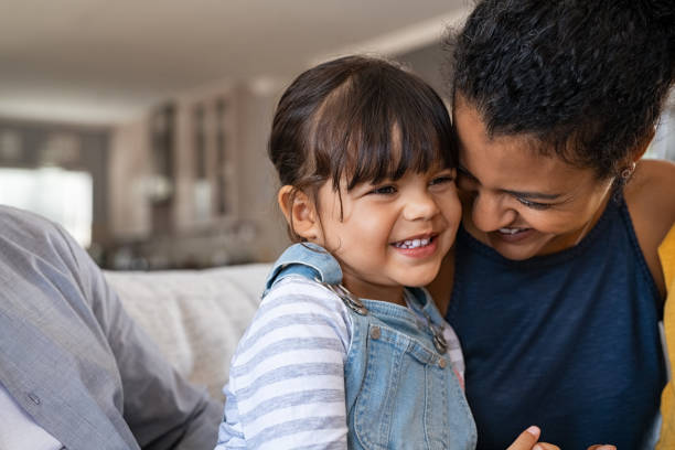 African lovely woman hugging shy daughter Beautiful black mother embracing little girl sitting on couch with copy space. Cute daughter hugging african american mother and smiling together. Happy latin mom jokes with her kid at home and playing together. family cheerful happiness mother stock pictures, royalty-free photos & images