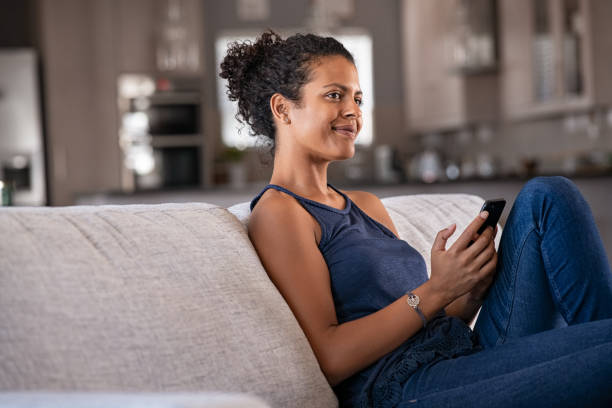 giovane donna nera che pensa mentre usa lo smartphone - young adult women african descent 30s foto e immagini stock