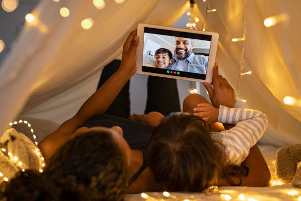 Mother and daughter in video call with father and son African mother and cute girl using digital tablet while lying in kid tent doing a video call with father and son. Woman and daughter using digital tablet for a videocall with middle eastern man and boy. Indian family in online conversation with each other during quarantine and social distancing. tent photos stock pictures, royalty-free photos & images