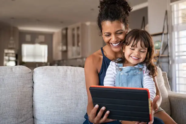 Photo of African smiling mother and happy daughter using digital tablet