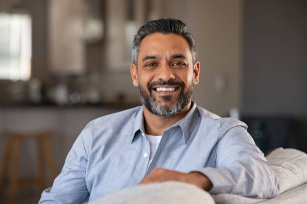 Portrait of happy indian man smiling at home Portrait of happy mid adult man sitting on sofa at home. Handsome latin man in casual relaxing on couch and smiling. Cheerful indian guy looking at camera. 40 44 years stock pictures, royalty-free photos & images
