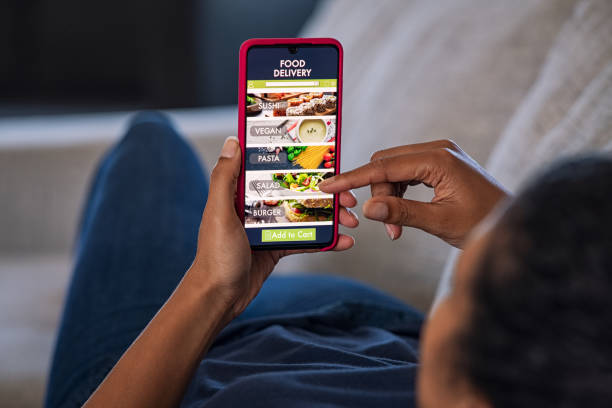 Woman ordering food online Woman lying on couch using food delivery app on smartphone. Close up of african woman hands holding cellphone and ordering food online. Girl using smart phone to get home delivered take away lunch. ordering stock pictures, royalty-free photos & images