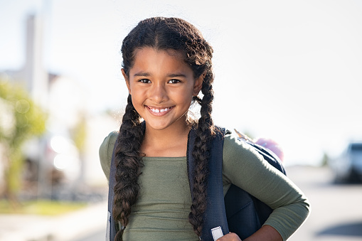 Portrait of happy indian girl with school bag standing outdoor. Little happy schoolgirl going to school, back to school and education concept. Beautiful cute mixed race female student smiling and looking at camera.