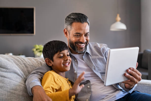 デジタルタブレットを使用してビデオ通話を行う父と息子 - digital tablet family father offspring ストックフォトと画像