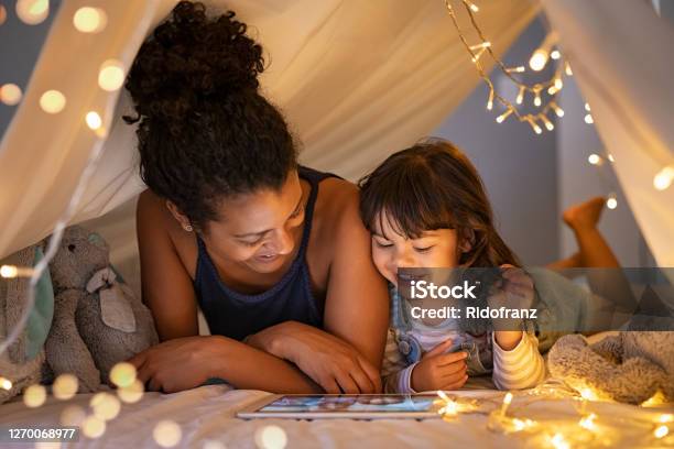 Mother And Daughter Using Digital Tablet Inside Illuminated Cozy Hut Stock Photo - Download Image Now