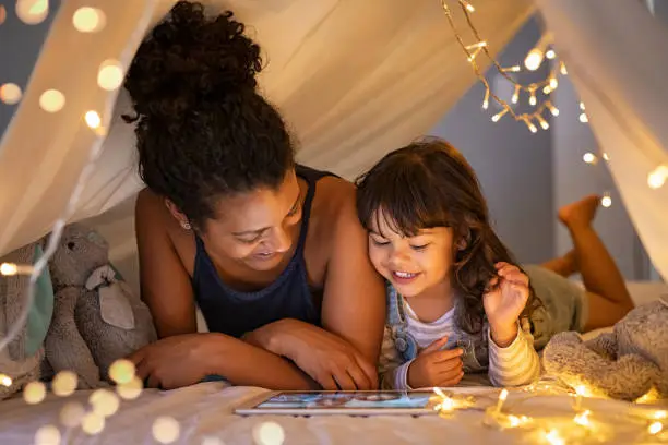 Photo of Mother and daughter using digital tablet inside illuminated cozy hut