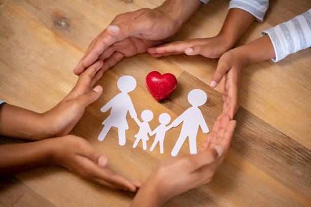 Family protection and care concept Close up hands of father, mother and daughters protecting family paper cutout with red heart. Hands of mixed race family with paper cutting and red heart shaped symbol stone on wooden background. Unity, insurance and love concept. heart hands multicultural women stock pictures, royalty-free photos & images