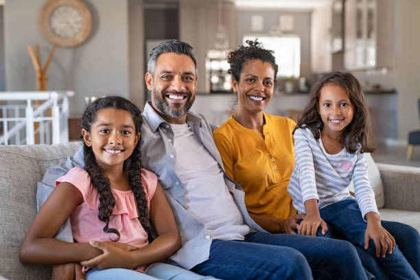 Happy multiethnic family sitting together Portrait of cheerful ethnic family at home sitting on sofa and looking at camera. Happy indian family with two children relaxing at home. Mixed race parents with their daughters in new home. 40 44 years photos stock pictures, royalty-free photos & images