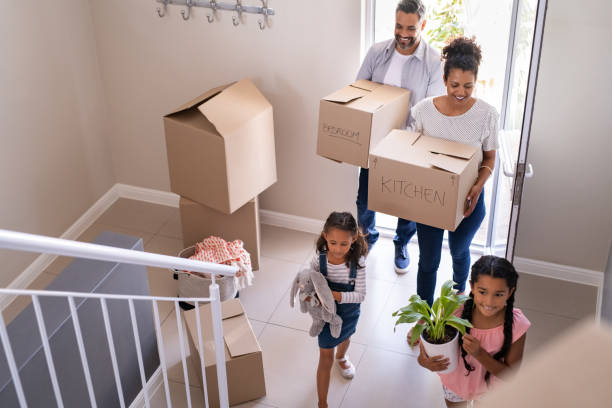 Multiethnic family moving in new home Ethnic family with two children carrying boxes and plant in new home on moving day. High angle view of happy smiling daughters helping mother and father with cardboard boxes in new house. Top view of excited kids having fun walking up stairs running to their rooms while parents holding boxes. new home stock pictures, royalty-free photos & images