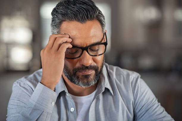 Stressed ethnic man with headache Frustrated middle aged man with hand on head sitting on couch at home. Close up face of stressed indian businessman wearing eyeglasses with eyes closed. Worried middle easter business man with terrible migraine, overload and overworked concept. edgy man stock pictures, royalty-free photos & images