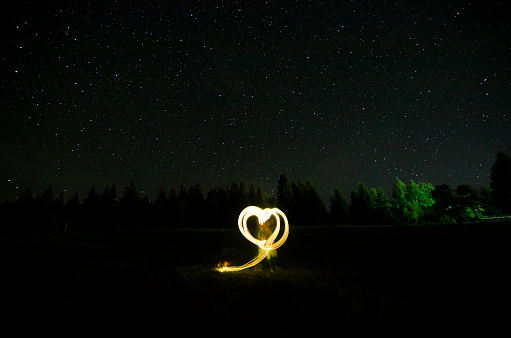 light writing in the shape of a heart with a starry sky in the background. captured in the mountains