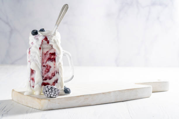 frullato di yogurt ai lamponi traboccante di bacche congelate - yogurt yogurt container strawberry spoon foto e immagini stock