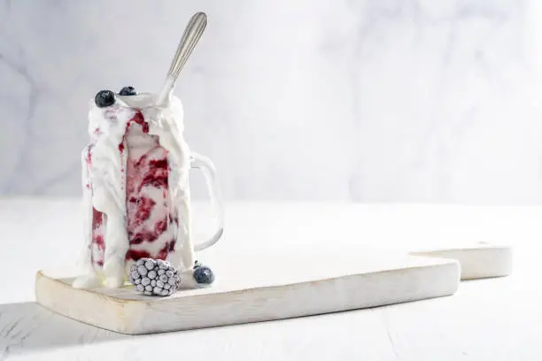 Raspberries yogurt smoothie overflow with frozen blueberries, blackberries and raspberries on a white table
