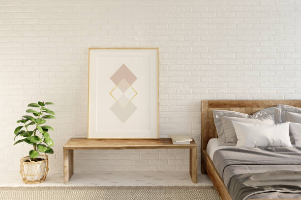 istock Bright interior with brick wall and beige carpet on a white wooden floor. Vertical poster stands on a wooden bench between a plant in an openwork basket and a wooden bed. Front view. 1270076438