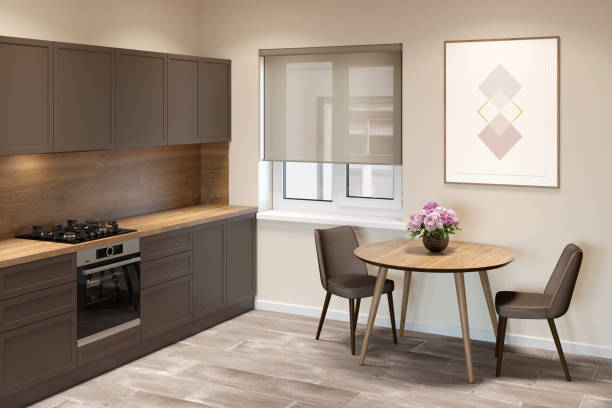 istock Beige kitchen interior with a window with blinds between a round table with two chairs and kitchen cabinets. There is a vertical poster on the wall above the table. 1270076654