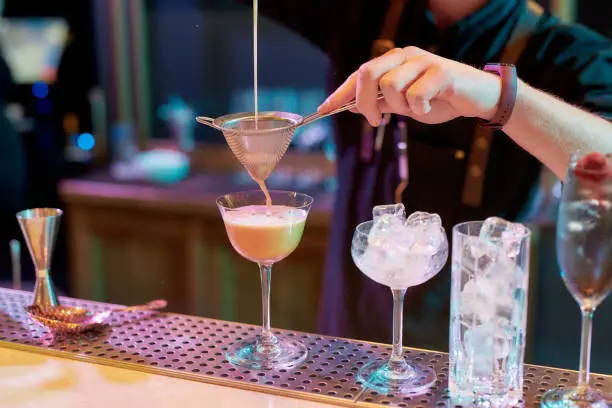 Photo of Close up of male bartender pouring, mixing ingredients while making cocktail alcoholic drink at the bar counter in the night club