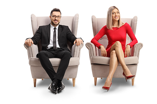 Elegant young man and woman sitting in armchairs isolated on white background