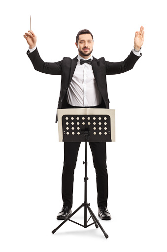 Full length portrait of a musical conductor with a baton performing with a notebook on a stand isolated on white background