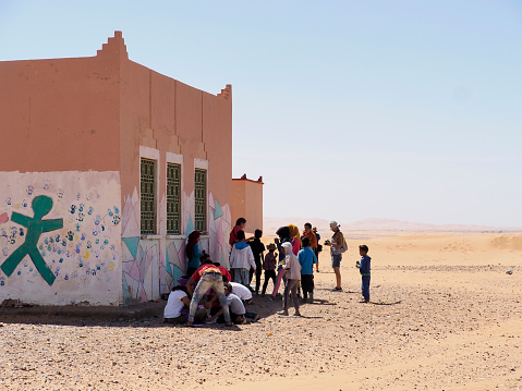 Tissardmine, Morocco, September, 20, 2019 Group of Moroccan children playing in the shade outside their desert school, waiting to start classes in the middle of the Sahara summer.