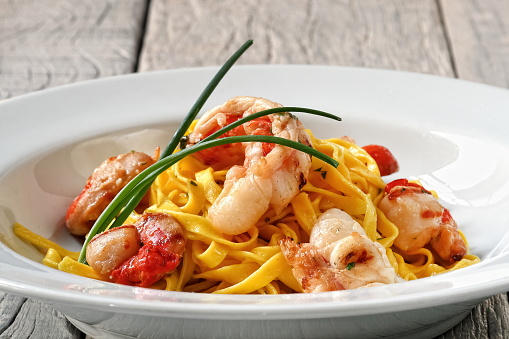 A serving of Salmon Spaghetti in a dark round bowl on a wooden background