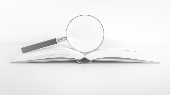 open book with a magnifying glass on the white desk high key_16_9 format_black and white