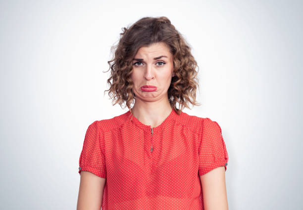 ritratto di una giovane bella ragazza in abito rosso con un'espressione emotiva di risentimento, su sfondo chiaro. - women crying sadness humor foto e immagini stock