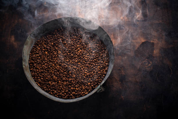 Medium Roasted Coffee beans smoky in roasting pan on wood Medium Roasted Coffee beans smoky in roasting pan on wooden background texture cafe stock pictures, royalty-free photos & images