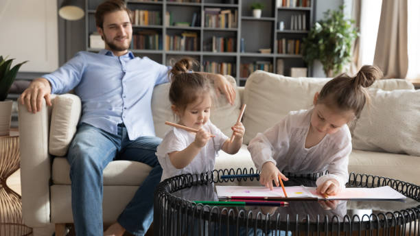 istock Small sisters drawing pictures while father resting on sofa. 1270093642