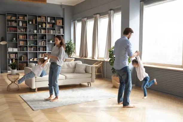 Photo of Energetic young couple twisting daughters in air.