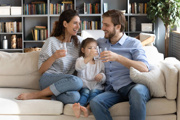 feliz pareja joven padres enseñando a la pequeña hija beber agua clara. - distilled water fotografías e imágenes de stock