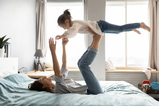 Photo of Young smiling mommy holding small kid daughter on straight legs.