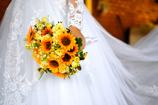 A stunning wedding bouquet made of Sunflowers, held by the bride, dressed in her white dress.