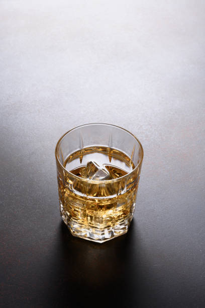 istock One shot of whiskey with ice cube on dark brown background. 1270095049