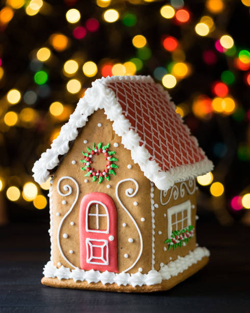 Gingerbread house with lights of Chrismtas decorated fir tree in background, selective focus