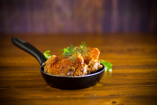 chicken legs fried in oil in a pan, on a wooden table